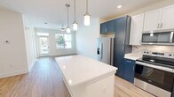 Located at 200 Brooklawn St in Farragut, TN, this well-appointed one-bedroom, one-bathroom unit offers a thoughtfully designed single-level layout. The open-concept kitchen is a standout feature, showcasing a striking two-tone design with bold navy lower cabinetry paired with crisp white upper cabinets, a marble-style tile backsplash, quartz countertops, and a full suite of stainless steel appliances including a range, microwave, dishwasher, and French door refrigerator. A large center island with pendant lighting bridges the kitchen and living area seamlessly. The living room is bright and airy, featuring light hardwood-style flooring, a ceiling fan, and large windows with an exterior door that fill the space with natural light and outdoor views. The bedroom offers plush carpeting, a ceiling fan, and a generous window. The bathroom provides a clean, functional design with dark wood vanity cabinetry, quartz countertops, a large mirror with brushed nickel lighting, and a tub-shower combination. A dedicated in-unit laundry room includes a full-size washer and dryer. Light hardwood flooring flows through the main living areas, tying together the home's modern, cohesive aesthetic.
