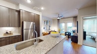 This well-appointed single-floor residence offers a thoughtfully designed open-concept layout that seamlessly connects the kitchen, dining, and living areas. The kitchen serves as a central hub, showcasing dark wood cabinetry extending to the ceiling, granite countertops, a generous island with an undermount sink, and a full suite of stainless steel appliances including a refrigerator, range, and microwave. Warm wood-look flooring runs throughout the main living areas, complementing the bright, neutral color palette.

The living area flows naturally from the kitchen, featuring a ceiling fan, recessed lighting, and large windows and a sliding glass door that invite abundant natural light and offer views to an outdoor balcony. The bedroom is a comfortable retreat, complete with plush carpeting, a ceiling fan, large windows with blinds and drape treatments, and direct access to both a walk-in closet and an en-suite bathroom. The bathroom is finished with granite countertops on a dark-toned vanity, a glass-enclosed walk-in shower with tile surround, and wood-look flooring that ties the space together cohesively. Recessed lighting throughout the unit contributes to a clean, contemporary ambiance.