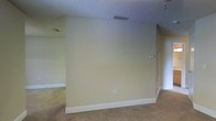 This single-floor space presents a clean and straightforward layout designed for comfortable everyday living. The interior features warm, neutral-toned walls painted in a soft cream hue that lend a calm and inviting atmosphere throughout. Underfoot, wall-to-wall carpeting adds warmth and comfort to the living areas, complementing the understated color palette. The textured popcorn ceiling adds a classic finish overhead, while white baseboards provide a crisp contrast along the floor line. Ventilation is well-considered, with ceiling vents integrated throughout to ensure consistent airflow. A thermostat is conveniently mounted on the wall, offering easy climate control. The open wall space provides excellent flexibility for furniture arrangement and décor, making the space highly adaptable to a variety of uses. Overall, the space offers a neutral, move-in-ready canvas with a simple and functional design that allows new occupants to personalize it to their tastes.