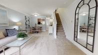 This two-story home is thoughtfully designed with a flowing layout that connects the main living spaces on the ground floor. The open main level features a spacious living room anchored by a classic white-manteled fireplace with a black surround, a wall-mounted television above, and a sliding glass door that floods the room with natural light while offering views of the surrounding greenery. Crown molding and neutral carpeting carry throughout, reinforcing a clean, cohesive aesthetic.

The dining area sits adjacent to the living room and connects directly to the kitchen, which is outfitted with warm honey-toned cabinetry, light tile flooring, and a full suite of black appliances including a range, dishwasher, microwave, and refrigerator. A pass-through opening maintains visual connectivity between the kitchen and dining space. A powder room on the main level features tile flooring, a wood vanity, and a bold slate-blue accent wall.

A carpeted staircase leads to the upper level, where the bedrooms are located. Each bedroom features plush carpet, natural light from windows with decorative curtains, and ample closet space via sliding panel doors. A full bathroom on this level includes a tub-shower combination with tile surround.