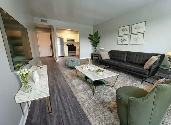 Sala de estar y comedor abiertos con sofá negro, mesa de mármol, silla verde, arte en la pared y cocina con electrodomésticos de acero inoxidable. - Prime at Gardenside