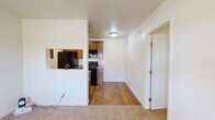 This single-floor unit offers a well-organized layout that balances function and comfort across its living spaces. The living area is finished with plush wall-to-wall carpeting and connects seamlessly to the kitchen via a pass-through window cutout, creating an open and communicative feel between the two spaces. A ceiling fan with integrated lighting keeps the area comfortable and well-lit.

The kitchen is equipped with black appliances, including a refrigerator, an electric range, and an over-the-range microwave. Warm-toned hardwood flooring runs throughout the kitchen, complementing the medium-toned wood cabinetry and granite-style countertops. The layout is efficient, making good use of the available space for both cooking and storage.

The bedrooms are carpeted and bright, each featuring a ceiling fan and windows dressed with horizontal blinds that allow for adjustable natural light. The rooms offer a clean, neutral canvas suitable for a variety of furnishing styles.

The bathroom is neatly appointed with hardwood flooring, a wood vanity cabinet topped with granite-style counters, a white basin sink, and a full tub-shower combination with light-toned surround panels and brushed nickel fixtures and towel bars. The overall aesthetic throughout the unit is clean, neutral, and move-in ready.