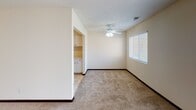 This single-floor unit offers a practical and well-organized layout with distinct living, sleeping, and cooking areas connected by a clear, functional flow. The galley-style kitchen is outfitted with ample white cabinetry lining both walls, providing generous storage and counter space. A double sink, full-size refrigerator, and built-in appliances complete the kitchen, which features tile flooring and a textured ceiling with overhead lighting. The kitchen opens directly into the adjacent living and dining areas, creating an easy transition between spaces. The living area is carpeted and benefits from natural light streaming through a large sliding glass door fitted with vertical blinds, which leads out to a private wooden deck — a notable outdoor feature. Ceiling fans are present in multiple rooms, including the bedrooms, contributing to comfortable air circulation throughout. The bedrooms are carpeted and well-proportioned, each with a window offering views to the outside. The bathroom includes a full-size soaking tub and shower combination, a wide single-basin vanity with an extended mirror, and tile flooring. Throughout the unit, neutral tones and light-colored walls create a clean, bright ambiance suited to a variety of living arrangements.