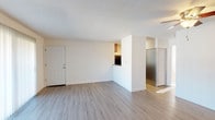 This single-floor unit offers a clean, functional layout designed for comfortable everyday living. The open living area is finished with light wood-style laminate flooring and features a ceiling fan, a textured ceiling, and a large sliding glass door that fills the space with natural light and provides access to an outdoor area. A half-wall partition separates the living space from the kitchen, which is equipped with rich wood cabinetry, granite-style countertops, stainless steel appliances including a refrigerator, microwave, and electric range, creating a practical and stylish cooking environment. The bedroom is carpeted for comfort and includes a generously sized reach-in closet with a full-width hanging rod, offering ample storage. The bathroom is neatly appointed with wood-style flooring, a combined tub and shower with built-in shelving, a curved shower rod, and a vanity with granite-style countertops and warm wood cabinetry. Throughout the unit, white walls and consistent flooring choices create a cohesive, light, and airy ambiance. The layout flows efficiently, making thoughtful use of every area within the space.