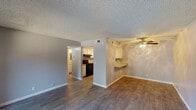 This single-floor residence offers a well-organized layout designed for comfortable everyday living. The main living area is open and airy, featuring durable wood-look flooring, soft gray walls, a textured ceiling, and a ceiling fan with light fixture. A sliding glass door floods the space with natural light and provides access to an outdoor area, offering views of the surrounding greenery.

The kitchen is efficiently designed with white cabinetry, a mosaic tile backsplash, a built-in black range, and an under-mount sink. A wraparound countertop extends into a breakfast bar that connects the kitchen to the living and dining areas, making it ideal for casual dining or food preparation.

The primary bedroom is carpeted for warmth and comfort, featuring an open closet with a hanging rod for ample storage. A second carpeted bedroom includes a window that allows natural light to filter in. Both bedrooms share neutral gray walls and textured ceilings consistent with the rest of the unit.

The bathroom is clean and functional, featuring a combination shower and bathtub, a toilet, and wood-look flooring that matches the main living areas. Utility space, visible through the bedroom, provides additional convenience. Throughout the unit, consistent gray-toned walls, white trim, and cohesive flooring choices create a clean, modern aesthetic.
