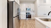 Located at 104 Herrings Green Loop in Mooresville, NC, this single-story, one-bedroom, one-bathroom home offers a thoughtfully designed layout that maximizes every square foot. The open-concept kitchen and living area serves as the heart of the home, featuring light wood-tone flooring, white shaker cabinetry, a subway tile backsplash, and a full suite of stainless steel appliances including a refrigerator, range, and microwave. A central island with a white quartz countertop, undermount sink, and pendant lighting adds both function and style, complemented by matte black hardware throughout. The living area receives ample natural light through large windows and a glass-paneled door that opens to the outdoors. The bedroom is comfortably sized, finished with plush carpet, a ceiling fan, and a window with outdoor views. A dedicated walk-in closet with wire shelving provides generous storage. The full bathroom is appointed with a white vanity, quartz countertop, tub-shower combination with tiled surround, and wood-look flooring. Clean neutral tones, consistent finishes, and an efficient floor plan give this home a cohesive, modern feel throughout.