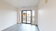 This contemporary 1-bedroom, 1-bathroom unit offers a well-designed, single-floor layout that maximizes every square foot. The open-concept kitchen and living area serves as the heart of the space, featuring crisp white shaker cabinetry with matte black hardware, light quartz countertops, a subway tile backsplash, and a full suite of stainless steel appliances including a refrigerator, range, microwave, and dishwasher. A peninsula with an undermount sink and stylish pendant lighting adds both function and visual appeal, flowing seamlessly into the living area. Wood-look plank flooring runs throughout the main living spaces, complemented by large black-framed windows and a sliding glass door that floods the area with natural light and provides access to an outdoor balcony with neighborhood views. The bedroom is a comfortable, carpeted retreat featuring floor-to-ceiling windows on two walls, offering bright, open views of the surrounding landscape. A dedicated closet with built-in hanging rods provides practical storage. The bathroom is finished with large-format tile flooring, a white vanity with black hardware, a well-lit mirror, and a walk-in shower with clean white tile surround. A hallway connects all spaces efficiently, completing this thoughtfully designed modern residence.