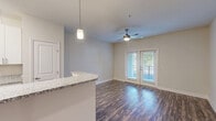This well-appointed one-bedroom, one-bathroom residence at 120 Buckhill Village Dr in Burlington, NC offers a thoughtfully designed single-floor layout. The open-concept living area seamlessly connects the kitchen, dining, and living spaces, creating an airy and functional atmosphere. Rich wood-look plank flooring runs throughout the main living areas, complemented by neutral-toned walls that enhance the bright, clean aesthetic.

The kitchen is a standout feature, showcasing white shaker-style cabinetry, granite-look countertops, and a full suite of stainless steel appliances including a refrigerator, electric range, microwave, and dishwasher. A peninsula with an integrated sink provides additional prep space and doubles as a casual dining counter. Pendant lighting adds a modern touch overhead. The living area opens directly to a private patio through French doors, with a ceiling fan adding comfort.

The bedroom offers plush carpeting, a ceiling fan, and multiple closets for generous storage. The bathroom includes a full tub-shower combination with chrome fixtures. A dedicated laundry room houses a full-size washer and dryer. Additional storage is provided through a pantry and multiple closets throughout the hallway, making this a practical and comfortable home.