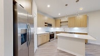 This single-story, one-bedroom, one-bathroom unit offers a well-designed open-concept layout with a neutral, modern aesthetic throughout. Light wood-look flooring extends across the main living areas, complementing the bright, airy feel created by recessed lighting and a clean white color palette.

The combined kitchen and living area serves as the heart of the unit. The kitchen is outfitted with flat-front light wood cabinetry, white quartz countertops, a classic subway tile backsplash, and a full suite of stainless steel appliances including a French door refrigerator, electric range, built-in microwave, and dishwasher. A large center island provides additional workspace and casual seating, while two glass pendant lights add a refined touch overhead.

The bedroom features plush carpet flooring, a ceiling fan with light, and a window fitted with blinds. It connects directly to the full bathroom, which includes a dual-sink vanity with wood cabinetry and quartz countertops, framed mirrors with track lighting above, and a glass-enclosed walk-in shower with marble-style tile surround.

Two walk-in closets equipped with wire shelving systems provide generous storage. The space also appears to include an in-unit washer and dryer area, adding everyday convenience.