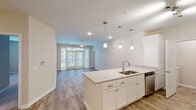 Located in Gulf Shores, Alabama, this three-bedroom, three-bathroom residence delivers a clean, modern aesthetic across a single-floor layout. The open-concept kitchen and living area forms the heart of the home, where wood-look flooring flows throughout and abundant natural light pours in through large French doors leading to an outdoor space. The kitchen is outfitted with white shaker-style cabinetry, a subway tile backsplash, stainless steel appliances including a refrigerator with ice maker, electric range, microwave, and dishwasher, and a generously sized island with a double sink and pendant lighting overhead — ideal for both meal prep and casual dining. The living area benefits from a ceiling fan and recessed lighting, creating a comfortable, well-lit environment. Each of the three bedrooms features plush carpeting, a ceiling fan, and windows with blinds that allow for natural light and privacy. The bathrooms are finished with classic hexagonal tile flooring, white subway-tiled tub surrounds, and vanities with clean countertops and brushed nickel fixtures. One bathroom features a wide vanity with sage-toned cabinetry and a well-lit mirror. Throughout the residence, neutral tones and consistent finishes create a cohesive and inviting atmosphere.