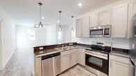 This single-floor, 3-bedroom, 2-bathroom residence offers a thoughtfully designed layout that balances functionality and comfort. The modern kitchen serves as a focal point, featuring gray shaker-style cabinetry, dark granite countertops, and a full suite of stainless steel appliances including a range, microwave, dishwasher, and refrigerator. A peninsula with a matching granite surface opens to the adjacent living area, while stylish glass pendant lights provide warm, focused illumination overhead. Wood-look luxury vinyl flooring runs throughout the main areas, lending a clean and cohesive aesthetic. The three bedrooms are carpeted and bright, each equipped with a ceiling fan and natural light from windows overlooking the surrounding neighborhood. The primary bedroom is a comfortable size and is paired with an en-suite bathroom that includes a soaking tub, a vanity with granite countertop, and direct access to a walk-in closet with built-in shelving. The second bathroom mirrors the same design, featuring a tub/shower combo and granite vanity. A dedicated closet space with double sliding doors accommodates laundry hookups, adding practical convenience. Clean white walls, recessed lighting, and consistent finishes throughout give the home a fresh, move-in-ready feel.
