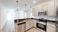 This single-floor, 3-bedroom, 2-bathroom residence offers a thoughtfully designed layout that balances functionality and comfort. The modern kitchen serves as a focal point, featuring gray shaker-style cabinetry, dark granite countertops, and a full suite of stainless steel appliances including a range, microwave, dishwasher, and refrigerator. A peninsula with a matching granite surface opens to the adjacent living area, while stylish glass pendant lights provide warm, focused illumination overhead. Wood-look luxury vinyl flooring runs throughout the main areas, lending a clean and cohesive aesthetic. The three bedrooms are carpeted and bright, each equipped with a ceiling fan and natural light from windows overlooking the surrounding neighborhood. The primary bedroom is a comfortable size and is paired with an en-suite bathroom that includes a soaking tub, a vanity with granite countertop, and direct access to a walk-in closet with built-in shelving. The second bathroom mirrors the same design, featuring a tub/shower combo and granite vanity. A dedicated closet space with double sliding doors accommodates laundry hookups, adding practical convenience. Clean white walls, recessed lighting, and consistent finishes throughout give the home a fresh, move-in-ready feel.