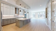 This contemporary 1250 square foot apartment offers a blend of comfort and style across a single floor. The space is thoughtfully designed with two bedrooms and two bathrooms, providing ample room for residents and guests. The primary bedroom is generously sized at 180 square feet, ensuring a luxurious retreat.

The living area is characterized by its openness and abundance of natural light, courtesy of large windows that offer urban views. Light-toned wood flooring throughout creates a sense of continuity and enhances the apartment's modern aesthetic. The kitchen area, visible in the image, features sleek cabinetry in contrasting colors, with upper white cabinets and lower blue-grey units. A built-in wine refrigerator adds a touch of sophistication.

Custom window treatments provide privacy and light control, while recessed lighting ensures even illumination throughout the space. The neutral color palette of whites and greys creates a calming atmosphere and allows for personalization. With two closets, the apartment offers practical storage solutions to maintain a clutter-free environment. This well-designed urban dwelling seamlessly combines functionality with contemporary style, making it an ideal home for those seeking a modern living experience.