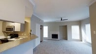 This single-floor residence offers a well-designed open-concept layout that seamlessly connects the kitchen and living areas. The living room is a standout space, centered around a classic tiled fireplace flanked by windows that invite generous natural light throughout the day. A ceiling fan overhead adds both functionality and a finishing touch to the room's clean aesthetic. Soft, plush carpeting covers the living area floor, contributing to a warm and comfortable ambiance.

The kitchen area features a granite-topped breakfast bar or counter that flows into the living space, creating a natural divide while maintaining the open feel. White cabinetry and modern hardware give the kitchen a fresh, contemporary look, and a small decorative plant on the counter adds a touch of life to the space.

Crown molding runs along the ceiling, adding an elegant architectural detail that elevates the overall design. The neutral gray-toned walls throughout provide a versatile backdrop that complements a wide range of furnishing styles. Multiple windows ensure the space remains bright and airy, reinforcing the sense of openness across this thoughtfully laid-out single-level home.