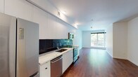 Located in Portland's vibrant NW Raleigh Street corridor, this single-floor unit offers a thoughtfully designed open-concept layout that seamlessly connects the kitchen and living areas. Rich, dark hardwood flooring runs throughout the main living space, adding warmth and depth to the otherwise clean, modern aesthetic defined by crisp white walls and smooth ceilings.

The kitchen is a standout feature, outfitted with sleek, high-gloss white cabinetry that extends to the ceiling for generous storage. A striking dark tile backsplash provides bold contrast against the white marble-style countertops and undermount stainless steel sink. Stainless steel appliances, including a refrigerator, dishwasher, range, and microwave, complete the contemporary culinary space.

The open living area benefits from natural light streaming in through a large window, offering a view of mature greenery outside — a refreshing touch of nature. The layout also accommodates an in-unit washer and dryer, adding everyday convenience.

The bathroom is finished in a clean, neutral palette with light tile flooring, a full soaking tub with shower, a wide vanity mirror, and recessed lighting, creating a bright and functional space. The overall ambiance of the unit is modern, minimal, and move-in ready.