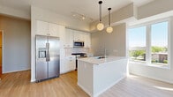 Located at 177–181 E First St in Elmhurst, Illinois, this single-floor, 2-bedroom, 2-bathroom unit offers a thoughtfully designed layout with modern finishes and a cohesive neutral palette throughout. The kitchen serves as a standout feature, showcasing white shaker cabinetry extending to the ceiling, a white quartz peninsula with an undermount sink, and a full suite of stainless steel appliances including a French door refrigerator, gas range, built-in microwave, and dishwasher. Globe pendant lights hang above the peninsula, adding a contemporary touch, while light hardwood-style flooring and large windows invite natural light from outdoor views of the surrounding Elmhurst streetscape. A clean hallway with louvered closet doors and black hardware connects the living areas to the private bedrooms, both of which feature plush carpet flooring and large windows that bring in ample daylight and neighborhood views. Each bedroom includes closet storage. The two bathrooms are finished with light wood-look flooring or tile, white vanities with quartz countertops, large framed mirrors with black accents, and clean, minimalist fixtures. The overall design presents a consistent modern aesthetic with black hardware details, soft warm tones, and an efficient, well-organized floor plan.