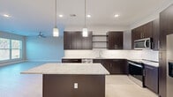 Located at 1110 Metropolitan Ave in Summerville, SC, this contemporary single-floor home offers a thoughtfully designed layout with two bedrooms, one bathroom, and a dedicated closet. Light hardwood-style flooring flows consistently throughout the space, creating a clean and cohesive aesthetic.

The kitchen is a standout feature, showcasing rich dark espresso cabinetry, open shelving, a white tile backsplash, and a large granite-topped island with a bold navy blue base. Stainless steel appliances, including a refrigerator, range, microwave, and dishwasher, complete this well-appointed space. Pendant lighting above the island adds warmth and style. A sliding barn door is also visible from the kitchen area, adding a modern touch.

Both bedrooms are bright and airy, benefiting from large windows that invite generous natural light and outdoor views. Ceiling fans are present in the main living and bedroom areas for added comfort. The bedrooms feature neutral warm-toned walls and clean white baseboards, contributing to a calm, move-in-ready atmosphere.

The bathroom is well-finished with light tile flooring, a tub-shower combination enclosed by sleek sliding glass doors, and brushed nickel fixtures. The overall design of this home balances modern finishes with a comfortable, functional layout suited for everyday living.