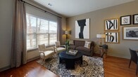 Located at 95–111 University Ave in Westwood, Massachusetts, this single-floor residence offers a thoughtfully designed layout that balances contemporary style with everyday functionality. The living room is anchored by large windows dressed with patterned drape panels, allowing generous natural light to fill the space while providing views of the surrounding neighborhood. Warm hardwood flooring runs throughout, complementing the neutral, earthy wall tones that lend a cohesive and welcoming ambiance.

The kitchen is a standout feature, equipped with rich dark-stained cabinetry that extends to the ceiling, stainless steel appliances including a range, built-in microwave, and refrigerator, and a granite-topped island with an undermount sink. Pendant lighting and track lighting illuminate the space effectively, while a tile backsplash adds a clean, polished finish. The kitchen opens toward a dining area, enhancing the open feel of the common spaces.

The bedroom is a calm retreat, carpeted for comfort and brightened by a large window with outdoor views. It connects to a well-appointed bathroom featuring a dual-sink vanity with dark cabinetry, a wide mirror, tile flooring, and a separate water closet, providing both practicality and an elevated aesthetic throughout.
