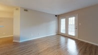 This single-floor residence presents a cohesive, functional layout with consistent design choices throughout. The living area features light hardwood-style flooring and neutral beige walls, creating a bright, open atmosphere. A set of French doors along one wall allows natural light to filter in and provides outdoor access, enhancing the airy feel of the space.

Adjacent to the living area, the kitchen is designed in a galley style with dark espresso cabinetry, white countertops, and stainless steel appliances including a refrigerator and microwave. Open shelving adds a modern touch, while a peninsula with a built-in sink connects the kitchen to the living space, facilitating an open-concept flow. Light hardwood-style flooring continues seamlessly throughout these main areas.

The bedroom offers plush carpeting for added comfort and features a ceiling fan with integrated lighting. A window provides natural light and views of surrounding greenery, giving the room a calm, restful ambiance.

The full bathroom is well-appointed with dark wood vanity cabinetry, white countertops, brushed nickel fixtures, and a combination tub and shower with white tile surround. Light hardwood-style flooring ties the bathroom's design together with the rest of the home.