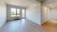 This contemporary single-floor unit showcases a clean, modern design with a thoughtful open-concept layout. The kitchen is well-appointed with light wood cabinetry extending to the ceiling, stainless steel appliances including a refrigerator, range, microwave, and dishwasher, and a sleek white quartz countertop island that doubles as a breakfast bar. Light hardwood-style flooring flows seamlessly through the kitchen and living areas, creating a bright and cohesive aesthetic. Recessed lighting throughout ensures consistent illumination across the space.

The open living area is generously proportioned, offering flexibility for furniture arrangement, and transitions easily from the kitchen. Large windows invite abundant natural light and frame views of the surrounding urban neighborhood.

The carpeted bedroom provides a comfortable retreat, featuring a ceiling fan, a large window with sweeping city views, and direct access to a spacious walk-in closet with built-in shelving. A second room, also accessible from the main living area, offers additional flexible living space.

The full bathroom is finished with a wide vanity topped with white countertops, light wood cabinetry, a large mirror, and a tub-shower combination, all set against a neutral, light-toned floor. The overall design palette — soft whites, light woods, and warm neutrals — gives the entire unit a fresh, contemporary feel.