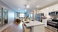 Located at 2480 Cherry Laurel Dr in Sanford, Florida, this well-appointed single-story residence offers a thoughtfully designed open-concept layout with modern finishes throughout. The kitchen is a standout feature, showcasing crisp white shaker cabinetry, stainless steel appliances including a refrigerator, microwave, and range, and a generously sized island with quartz countertops and seating for casual dining. Stylish globe pendant lights hang above the island, adding a contemporary touch. Rich wood-look flooring flows seamlessly from the kitchen into the open living area, which is bathed in natural light from multiple windows and features a ceiling fan for year-round comfort. The living space offers a warm, inviting ambiance with neutral tones and ample room for relaxed entertaining. The bedrooms are carpeted and serene, with large windows allowing abundant natural light and ceiling fans providing comfort. One bedroom features a striking green accent wall, adding a bold design element. The bathroom is finished with large-format marble-look tile flooring, a clean white vanity with an integrated sink, and a walk-in closet visible in the background, adding practical storage to the elegant space. Overall, this residence combines contemporary design with comfortable livability in a cohesive, light-filled environment.