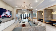 Located at 4 Tuscan Blvd in Salem, New Hampshire, this single-floor amenity space offers a thoughtfully designed environment that blends contemporary aesthetics with functional comfort. The welcoming lobby lounge serves as the heart of the space, anchored by a sculptural branch-like chandelier and furnished with a generous sectional sofa, accent chairs, and a large wall-mounted television set against a slatted wood feature wall. Light-toned tile flooring flows throughout, unifying the various zones seamlessly. An archway framed in warm wood slat detailing leads to a secondary lounge area centered on a dramatic floor-to-ceiling marble fireplace wall with gold veining, flanked by curved upholstered armchairs. A dedicated café-style dining area features bistro-height tables, mixed upholstered seating, warm pendant lighting, and a wood-paneled ceiling, with natural light entering through large windows. A cozy semi-private booth nook, lined with textured padded walls and topped with a sculptural pendant light, provides an intimate setting for meetings or casual conversation. Curated artwork is displayed throughout the corridors and common areas, adding cultural depth to the space. A fitness center, accessible via glass-paneled doors, completes the amenity offering. The overall design is modern, warm, and polished.