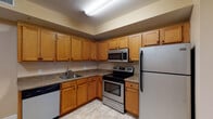 This single-floor residential unit offers a well-organized and practical layout designed for comfortable everyday living. The kitchen serves as a functional centerpiece, featuring warm honey-toned wood cabinetry with ample upper and lower storage, granite-look countertops, and a full suite of stainless steel appliances including an electric range, over-the-range microwave, refrigerator, and dishwasher. Light-toned tile flooring completes the kitchen's clean, easy-to-maintain aesthetic.

The living area showcases rich hardwood flooring that adds warmth and character to the space. A standout feature is the triple-panel window arrangement dressed with wood-toned blinds, allowing generous natural light to fill the room and creating an inviting, airy atmosphere.

The bathroom is thoughtfully appointed with a vanity featuring wood cabinetry and a stone-look countertop, a standard tub and shower combination with chrome fixtures, and durable stone-pattern tile flooring. Warm yellow-toned walls contribute a cozy, welcoming feel.

Overall, the unit presents a cohesive design aesthetic with neutral wall tones, practical finishes, and functional spaces that balance utility and comfort throughout.