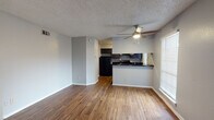 This single-floor unit offers a thoughtfully designed layout that balances open-concept living with defined private spaces. The main living area is anchored by rich wood-style flooring that extends throughout, a ceiling fan overhead, and a tiled fireplace that serves as a natural focal point. Natural light filters in through blinded windows, lending the space a bright and welcoming ambiance.

The kitchen is seamlessly connected to the living area via a half-wall breakfast bar, providing both functional separation and an open feel. It features dark espresso cabinetry reaching to the ceiling, dark granite-style countertops, and a full suite of black appliances including a refrigerator, range, and built-in microwave. The efficient layout makes excellent use of the available space.

A hallway off the kitchen leads to the private areas of the home, including a carpeted bedroom equipped with a ceiling fan and a window for natural light. The bathroom is appointed with dark cabinetry, dark granite-style countertops, a large vanity mirror, and a shower-tub combination. Additional storage is provided by an overhead cabinet. Consistent neutral gray walls and clean white trim tie the entire space together for a cohesive, move-in-ready aesthetic.