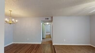 This single-floor residence offers a functional and well-organized layout across several rooms. The living area welcomes you with a ceiling fan fitted with a light kit, vertical blinds allowing natural light, and a transition from hardwood-style flooring to plush carpet. An adjacent dining area features an elegant chandelier and connects seamlessly to the kitchen through an open pass-through design.

The galley-style kitchen is outfitted with warm oak cabinetry, a tile mosaic backsplash, a double-basin sink, and white appliances including a coil-top range and refrigerator. Hardwood-style flooring runs throughout the kitchen and dining area, adding warmth and cohesion.

A central hallway connects the private areas of the home, leading to multiple bedrooms, each carpeted and equipped with ceiling fans and vertical blinds that invite natural light. One bedroom features a closet with panel doors, while all bedrooms offer ample wall space and a calm, neutral color palette.

The unit includes two bathrooms. One features a single-sink vanity with a gray countertop, wood cabinetry, and hardwood-style flooring. The second bathroom mirrors this style with a full tub-and-shower combination, large mirror, and matching vanity. Textured ceilings are consistent throughout the space, adding a classic residential character.