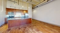 Located at 427 Pershing Ave in Davenport, Iowa, this two-bedroom, three-bathroom urban loft blends industrial character with modern finishes. The open-concept living and kitchen area immediately impresses with soaring ceilings, exposed ductwork, and whitewashed brick walls accented by a dramatic arched brick alcove. Hardwood flooring runs throughout, complementing the warm, loft-style aesthetic. A striking commercial-style glass garage door floods the main living space with natural light and adds an unmistakable urban edge. The kitchen features warm wood cabinetry, granite countertops, stainless steel appliances, and a generous island with pendant lighting overhead. The bedrooms are appointed with rich hardwood floors and distinctive sliding barn doors with black hardware, lending a rustic-modern contrast. The primary bedroom includes access to a dedicated walk-in closet. The three bathrooms are well-appointed, featuring granite-topped wood vanities throughout. The primary bath offers a frameless glass walk-in shower with large-format tile, while a secondary bath includes a full tub-shower combination with tile surround. A third half-bath features a white-painted exposed brick accent wall. This loft offers a compelling combination of historic architectural character and contemporary living essentials.