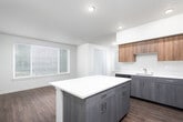 This well-appointed single-floor residence offers a thoughtfully designed layout that balances open communal spaces with private retreats. The kitchen serves as a centerpiece, showcasing two-tone cabinetry with warm wood upper cabinets and sleek gray lower cabinets, white quartz countertops, a full suite of stainless steel appliances including a refrigerator, range, microwave, and dishwasher, and a peninsula island ideal for casual dining or additional prep space. Rich, dark wood-look flooring flows seamlessly from the kitchen into the open living and dining area, which is bathed in natural light through large windows fitted with horizontal blinds.

A wide hallway connects the living spaces to the private areas of the home, where multiple bedrooms feature plush neutral carpeting, baseboard heating, and generous windows that invite natural light and outdoor views. Each bedroom is equipped with sliding panel closets, maximizing storage efficiency. 

The primary bathroom is notably spacious, offering a dual-sink vanity with gray cabinetry, white countertops, a large mirror, and a glass-enclosed shower. A secondary bathroom provides a full tub-shower combination with wood-look flooring and matching cabinetry. Throughout, the clean neutral palette and contemporary finishes create a cohesive, modern ambiance.
