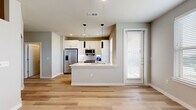 This well-designed single-story residence offers a thoughtful layout that maximizes every square foot. The open-concept kitchen and living area serves as the heart of the home, featuring light wood-tone flooring that flows seamlessly throughout. The kitchen is appointed with crisp white shaker cabinetry, a white quartz peninsula with an undermount sink, stainless steel appliances including a French door refrigerator, electric range, microwave, and dishwasher, and a classic white subway tile backsplash. Sleek black pendant lights hang above the peninsula, adding a modern contrast to the bright, neutral palette. A window near the kitchen allows natural light to fill the space. A hallway connects the living area to the private quarters, where the bedroom features light wood flooring, a ceiling fan, and a window with outdoor views, creating a calm and comfortable retreat. A dedicated closet provides convenient storage. The bathroom is finished with white subway tile surrounding a soaking tub and shower, a white vanity with ample drawer storage, and matching light wood-tone flooring. The bedroom also includes a separate carpeted area, ideal for a laundry or utility nook. Clean lines, neutral tones, and modern finishes define the overall aesthetic of this space.