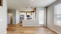 This well-designed single-story residence offers a thoughtful layout that maximizes every square foot. The open-concept kitchen and living area serves as the heart of the home, featuring light wood-tone flooring that flows seamlessly throughout. The kitchen is appointed with crisp white shaker cabinetry, a white quartz peninsula with an undermount sink, stainless steel appliances including a French door refrigerator, electric range, microwave, and dishwasher, and a classic white subway tile backsplash. Sleek black pendant lights hang above the peninsula, adding a modern contrast to the bright, neutral palette. A window near the kitchen allows natural light to fill the space. A hallway connects the living area to the private quarters, where the bedroom features light wood flooring, a ceiling fan, and a window with outdoor views, creating a calm and comfortable retreat. A dedicated closet provides convenient storage. The bathroom is finished with white subway tile surrounding a soaking tub and shower, a white vanity with ample drawer storage, and matching light wood-tone flooring. The bedroom also includes a separate carpeted area, ideal for a laundry or utility nook. Clean lines, neutral tones, and modern finishes define the overall aesthetic of this space.
