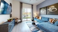This single-level 2-bedroom, 2-bathroom home delivers a well-designed floor plan with modern finishes throughout. The kitchen is a standout feature, showcasing two-tone cabinetry with slate-blue lower cabinets and crisp white uppers, white quartz countertops, a subway tile backsplash, stainless steel appliances, and a central island — all set over light-toned hardwood-style flooring that extends throughout the main living areas. The living room is bright and welcoming, featuring a ceiling fan, large sliding glass doors that open to an outdoor balcony, and generous natural light with views of the surrounding area. Both bathrooms are finished with the same hardwood-style flooring, gray vanity cabinetry, and white countertops, with each conveniently connected to a dedicated closet. The primary bedroom offers a comfortable, carpeted retreat with soft, neutral tones, while the second bedroom is equally well-proportioned. Two closets provide organized storage, including a walk-in closet with multiple hanging rods. A dedicated in-unit laundry area houses a full-size side-by-side washer and dryer with overhead shelving. The overall aesthetic is clean, contemporary, and cohesive throughout.