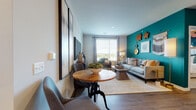 This thoughtfully designed single-floor residence blends modern style with vibrant pops of color throughout. The open-concept living and dining area serves as the heart of the home, highlighted by rich hardwood-style flooring, a bold teal accent wall adorned with decorative wall art, and generous windows that invite an abundance of natural light. A sliding glass door leads to a private balcony, offering outdoor views that extend the living space.

The kitchen is a standout feature, centered around a large island with seating for three, quartz countertops, and pendant lighting overhead. White upper cabinetry pairs with warm wood-tone lower cabinets, complemented by a full suite of stainless steel appliances and a classic subway tile backsplash.

The primary bedroom is distinguished by a warm amber accent wall, plush carpet flooring, and large windows dressed with floor-length drapes. Its en-suite bathroom features a double-sink vanity with wood-tone cabinetry, a walk-in glass shower, and hardwood-style flooring. A second bedroom offers a bright, neutral palette with ample natural light, served by a second full bathroom complete with a soaking tub and matching wood-tone vanity. Throughout the residence, cohesive finishes and intentional design details create a polished, contemporary ambiance.