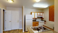 This single-floor residential unit offers a practical and well-organized layout designed for comfortable everyday living. The kitchen is a standout feature, equipped with oak-trimmed cabinetry paired with white cabinet doors, a white electric range, a full-size refrigerator, a built-in dishwasher, and a double stainless steel sink set into granite-look countertops. The kitchen opens to a dining and living area through a peninsula-style counter, creating a connected, open feel. Hardwood-style flooring runs through the kitchen and living areas, while a sliding glass door in the living space allows natural light to filter in and provides access to the outdoors. The bedrooms feature neutral-toned carpet flooring and windows fitted with vertical blinds, offering a quiet and private retreat. Closet space is included in at least one of the bedrooms. The bathroom is thoughtfully designed with accessibility in mind, featuring grab bars near the bathtub and sink, a shower-tub combination, a vanity with a wall-mounted mirror, and hardwood-style flooring. Throughout the unit, neutral wall tones and consistent finishes create a cohesive and functional living environment.