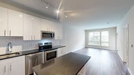 Located at 2803 Poag St in Alexandria, VA, this one-bedroom, one-bathroom unit offers a well-designed layout across a single floor. The open-concept kitchen and living area serves as the heart of the home, featuring rich hardwood-style flooring, track lighting, and a sleek modern kitchen outfitted with glossy white cabinetry, dark granite countertops, a subway tile backsplash, and a full suite of stainless steel appliances including a refrigerator, range, and built-in microwave. The living area flows naturally from the kitchen, providing a versatile and comfortable everyday space. The bedroom is carpeted for warmth and comfort, benefiting from large windows that invite generous natural light and offer views of the surrounding community. A door provides direct outdoor access, adding an airy quality to the room. The walk-in closet is outfitted with wire shelving and hanging rods, offering well-organized storage. The bathroom features large-format tile flooring, a walnut-toned vanity with an extended white countertop and wide mirror, and a full tub-shower combination enclosed with classic white subway tile. The overall design is clean, contemporary, and functional throughout.