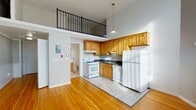 Located at 278 Main St in West Haven, CT, this studio offers a distinctive open layout enhanced by impressively tall ceilings that create a sense of spaciousness well beyond its footprint. A striking upper loft-level overlook with black metal railings adds architectural character and visual depth to the main living area below.

The kitchen is efficiently designed with warm honey-toned oak cabinetry, dark granite-style countertops, and a full suite of white appliances including a gas range, dishwasher, and refrigerator. A stainless steel sink and under-cabinet range hood complete the functional setup. The kitchen area transitions seamlessly into the open living space, which features rich hardwood flooring that extends throughout the unit.

A separate room with large windows fitted with vertical blinds provides a bright, versatile flex space suitable for a sleeping area, home office, or studio use. The walls include a distinctive tile wainscoting detail along the lower portion, adding a subtle design element.

The bathroom is clean and well-appointed, featuring a single-sink oak vanity with a framed mirror, a full tub/shower combination, and tile-style flooring. An electrical panel is conveniently accessible within the main living area. This studio combines practical functionality with unique architectural details in a well-located West Haven setting.