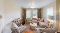This single-floor residence offers a cohesive layout with warm neutral tones, wood-style flooring, and plush carpeting that create a comfortable and welcoming atmosphere throughout. The living room serves as a central gathering space, featuring multiple windows with blinds that allow generous natural light and outdoor views. Ceiling fans enhance the room's comfort, and the space is well-suited for both relaxing and entertaining.

The kitchen is efficiently designed, outfitted with warm oak cabinetry extending to the upper walls for ample storage, dark granite-style countertops, and black appliances including a range, over-the-range microwave, dishwasher, and stainless refrigerator. A pantry closet provides additional storage convenience. Adjacent to the kitchen, a dedicated dining area accommodates a round table and seating beneath a window with natural light.

The bedrooms are carpeted and feature ceiling fans, windows with exterior views, and sufficient space for bedroom furnishings. The bathroom includes warm wood cabinetry, an illuminated vanity mirror, and wood-style flooring, offering a practical and tidy layout. Overall, the residence presents a functional and cohesive living environment with consistent finishes throughout.