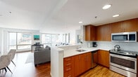 Located at 180 Brookline Ave in Boston's Fenway neighborhood, this well-appointed two-bedroom, two-bathroom residence offers a thoughtfully designed open-concept layout with rich hardwood flooring throughout. The kitchen serves as a central hub, featuring warm wood cabinetry, white quartz countertops, a breakfast bar peninsula, and a full suite of stainless steel appliances including a refrigerator, range, microwave, and dishwasher. It flows seamlessly into the combined living and dining area, which is bathed in natural light from expansive floor-to-ceiling windows offering urban views of the surrounding cityscape. The spacious primary bedroom is generously sized with large windows, ample closet space, and direct access to one of the two bathrooms. The second bedroom is well-proportioned and equally bright. Both bathrooms are finished with wood vanities, white countertops, and framed mirrors with brushed metal accents. A dedicated in-unit laundry room houses a full-size washer and dryer, adding a practical convenience. Clean white walls, recessed lighting, and a neutral palette throughout create a bright, modern ambiance well-suited to urban living in one of Boston's most vibrant neighborhoods.