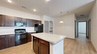 This 2-bedroom, 2-bathroom single-floor residence is thoughtfully laid out to maximize functionality and comfort. The open-concept kitchen and living area serves as the heart of the unit, featuring light wood-style flooring that runs consistently throughout the space. The kitchen is well-appointed with rich dark-brown cabinetry, light quartz-style countertops, black appliances including a refrigerator, range, and microwave, and a central island with additional cabinet storage below. A pendant light fixture hangs above the island, complementing the recessed lighting overhead. A decorative arched alcove adds a subtle architectural detail near the kitchen entry. The living area is generously proportioned, benefiting from a ceiling fan with light fixture, a glazed entry door, and windows dressed with horizontal blinds that allow natural light to filter in. The primary bedroom offers a comfortable footprint with its own ceiling fan, while the second bedroom is equally bright and well-sized. Both bedrooms feature the same consistent wood-style flooring and neutral white walls. The bathrooms are finished with matching dark cabinetry, light countertops, and a tub-shower combination. A dedicated closet provides additional storage within the unit.