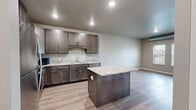 Located at 801 Kraewood Dr in Northfield, MN, this 1-bedroom, 1-bathroom unit offers a thoughtfully designed single-level layout with contemporary finishes throughout. The open-concept kitchen and living area serves as the heart of the unit, featuring rich dark-stained cabinetry, granite countertops, a central kitchen island, and a full suite of stainless steel appliances including a refrigerator, electric range, and dishwasher. Light wood-tone vinyl plank flooring runs throughout the main living areas, complementing the neutral gray wall palette and recessed lighting overhead. Exposed ductwork adds an industrial design accent visible in both the living and bedroom areas. The spacious bedroom is carpeted for comfort and features a large window that frames outdoor greenery, filling the room with natural light. A walk-in closet provides generous storage. The bathroom continues the unit's refined aesthetic with a granite-topped vanity, dark cabinetry with brushed nickel hardware, and a framed mirror. Clean lines and a cohesive neutral color scheme give the entire space a modern, move-in-ready feel suited for comfortable everyday living.