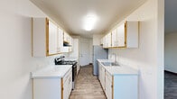 Located at 380 NW Gina Way in Beaverton, Oregon, this single-floor home offers five bedrooms and three bathrooms within a well-organized and functional layout. The galley-style kitchen is a standout feature, lined on both sides with white cabinetry accented by gold trim and equipped with white countertops, a stainless steel sink, an electric range, and a full-size refrigerator. Wood-look flooring runs throughout the kitchen and living areas, adding warmth and cohesion to the space. Natural light filters in through multiple windows, enhancing the clean, neutral color palette of white walls and light trim found throughout. The combined kitchen and living room area includes a ceiling fan and windows overlooking greenery, creating a pleasant, airy atmosphere. The five bedrooms feature plush carpeting and ample natural light, with several rooms offering closet space. Baseboard heating is present in the bedrooms, ensuring comfort year-round. The three bathrooms are finished with wood-look flooring, vanities with light fixtures, and clean, simple fixtures. A dedicated closet and hallway provide additional storage and connectivity between rooms. Overall, this home delivers a straightforward, comfortable living environment suited for a variety of needs.