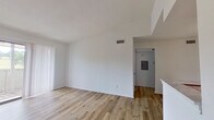 This thoughtfully laid-out 1-bedroom, 1-bathroom single-floor residence offers a clean, modern aesthetic throughout its efficiently utilized living space. The open living room is highlighted by light wood-tone flooring, crisp white walls, and a classic wood-burning fireplace with a white mantel, creating a warm focal point. A sliding glass door floods the room with natural light and provides direct access to a private balcony overlooking a green outdoor area. The kitchen is well-equipped with white cabinetry, marble-style countertops, stainless steel refrigerator, an electric range, dishwasher, and a built-in pantry closet, offering ample storage and functionality. An adjacent dining area with the same light hardwood flooring connects seamlessly to the kitchen. The bedroom is carpeted for comfort, features a ceiling fan, and is bathed in natural light from a large window. The full bathroom includes a tiled shower-tub combination, a vanity with marble-style countertop, and wood flooring, maintaining the clean, consistent style found throughout the home. A utility panel is conveniently located in the hallway. Overall, the space presents a bright, clean, and move-in-ready environment.
