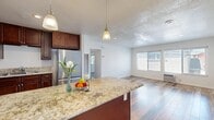 This single-story, 2-bedroom, 1-bathroom home offers a thoughtfully designed open floor plan that maximizes functionality and flow. The kitchen and living room share a connected open layout, anchored by a central island with a granite countertop and pendant lighting overhead. Rich, dark cabinetry pairs with stainless steel appliances, including a refrigerator and microwave, while the reclaimed wood-style flooring adds warmth and character throughout the entire home. The living room receives generous natural light through a large double window, creating a bright and welcoming atmosphere. A wall-mounted AC unit provides convenient climate control.

Both bedrooms continue the reclaimed wood-style flooring and feature ceiling fans, windows with views of greenery, and clean white walls. The primary bedroom includes mirrored sliding closet doors that enhance the sense of space. The second bedroom is comfortably sized and equally well-lit.

The bathroom is finished with full-height beige tile surrounding a soaking tub and shower combination, offering a clean and classic look. A hallway connects the private and shared areas of the home efficiently. Textured ceilings are present throughout, adding a subtle design detail consistent across the space.