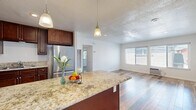 This single-story, 2-bedroom, 1-bathroom home offers a thoughtfully designed open floor plan that maximizes functionality and flow. The kitchen and living room share a connected open layout, anchored by a central island with a granite countertop and pendant lighting overhead. Rich, dark cabinetry pairs with stainless steel appliances, including a refrigerator and microwave, while the reclaimed wood-style flooring adds warmth and character throughout the entire home. The living room receives generous natural light through a large double window, creating a bright and welcoming atmosphere. A wall-mounted AC unit provides convenient climate control.

Both bedrooms continue the reclaimed wood-style flooring and feature ceiling fans, windows with views of greenery, and clean white walls. The primary bedroom includes mirrored sliding closet doors that enhance the sense of space. The second bedroom is comfortably sized and equally well-lit.

The bathroom is finished with full-height beige tile surrounding a soaking tub and shower combination, offering a clean and classic look. A hallway connects the private and shared areas of the home efficiently. Textured ceilings are present throughout, adding a subtle design detail consistent across the space.
