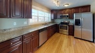 Located at 25 Mountain View in Lebanon, New Hampshire, this two-floor home offers a well-designed layout with quality finishes throughout. The kitchen is a standout feature, showcasing rich dark cherry cabinetry, granite countertops, and a full suite of stainless steel appliances including a range with microwave, dishwasher, and refrigerator with water dispenser. Light streams in through a multi-pane window above the sink, brightening the space alongside track lighting overhead. Warm bamboo hardwood flooring flows seamlessly through the main living areas, including an open hallway that connects the kitchen to the rest of the first floor. A staircase leads to the second level, where well-lit bedrooms feature the same warm hardwood floors, generous closet space, and large windows that invite natural light. The living area on the main floor includes a classic fireplace with a white mantel, adding a welcoming focal point to the room. Bathrooms across both floors are finished with matching dark cherry vanities topped with granite, brushed nickel fixtures, and clean tilework. The consistent use of quality materials — from the granite surfaces to the hardwood flooring — gives the entire home a cohesive and polished character.