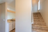 This two-story residence offers a thoughtfully laid-out floor plan with a warm, neutral color palette and durable hardwood-style flooring running throughout. The main level features a functional kitchen equipped with white cabinetry, speckled countertops, a stainless steel electric range with overhead ventilation, and a built-in sink area. Carpeted stairs with a handrail connect the two floors, with a window alongside the staircase drawing in natural light.

The upper level is a standout feature of the space, showcasing dramatic vaulted ceilings with exposed beams that lend an open, airy feel to the living and bedroom areas. Track lighting accents the high ceilings, and a sliding glass door provides access to a private balcony with outdoor views. Bedrooms on this level benefit from the elevated ceiling design, with one room featuring a striking angular roofline, a sliding-door closet, and a dedicated bathroom access. Additional bedrooms include closet storage and connect to a shared hallway.

Bathrooms are clean and functional, featuring speckled countertop vanities, large mirrors, and a full tub-shower combination with a small window for ventilation. The consistent use of neutral tones, white trim, and panel-style doors throughout creates a cohesive and inviting atmosphere across both floors.