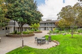 Located at 1032 W Remington Ave in Sunnyvale, CA, this thoughtfully designed residential community centers around an expansive, meticulously maintained courtyard that serves as the heart of the property. Sweeping concrete pathways wind through the grounds, connecting various outdoor gathering areas and framing a generous central lawn bordered by mature trees, ornamental plantings, and natural boulder accents.

The buildings present a classic mid-century aesthetic, featuring board-and-batten siding in a neutral gray palette, cedar shake accents, and dark navy entry doors. Stone-clad raised planting beds add texture and visual interest throughout the common areas, complementing the lush, layered landscaping that includes magnolias, redwoods, and a variety of flowering shrubs.

Multiple outdoor seating areas are distributed across the grounds, offering residents comfortable spaces to gather or unwind. A gated pool area, complete with covered pergola structures and lounge seating, provides a dedicated recreation zone along the perimeter of the property. Low-profile bollard lighting lines the pathways, ensuring the grounds remain inviting into the evening hours.

The overall ambiance is serene and park-like, with an abundance of greenery, natural materials, and carefully curated landscaping creating a tranquil retreat within a vibrant Silicon Valley neighborhood.