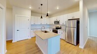 Located at 2700 Emerald Green Way in Knoxville, TN, this single-floor, 2-bedroom, 2-bathroom home offers a clean, modern design with thoughtful finishes throughout. The open-concept kitchen and living area serves as the heart of the home, showcasing crisp white cabinetry with matte black hardware, light quartz countertops, a classic subway tile backsplash, and a central island with a built-in sink and pendant lighting overhead. Stainless steel appliances — including a refrigerator, range, and microwave — complete the sleek kitchen. Light hardwood-style flooring runs throughout the main living areas, creating a bright and cohesive aesthetic. Both bedrooms are carpeted and comfortably sized, with natural light provided by windows overlooking the exterior. One bedroom features a sliding double-door closet, while the other includes a spacious walk-in closet with wire shelving for organized storage. Each bathroom is finished with light wood-style flooring, a tub/shower combo, vanity with white cabinetry, and matte black fixtures and accessories. Additional functional spaces include a dedicated laundry room, pantry, utility room, and hallway. The home's neutral palette and modern finishes lend a clean, move-in-ready feel throughout.